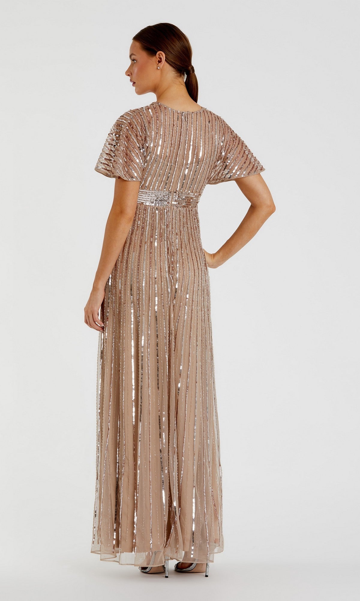 A woman is elegantly posed from the back against a light gray background, wearing the Long Formal Dress: Mac Duggal 94204—a floor-length, champagne-colored gown with sequin beading and short sleeves.